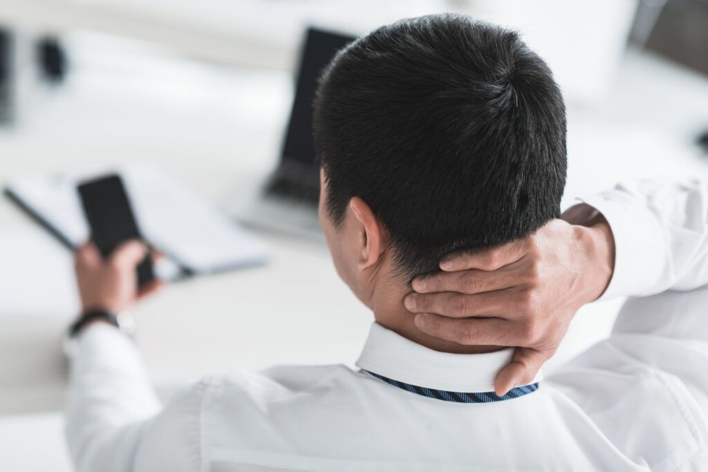 a man with his hand on his neck as he looks at his cell phon