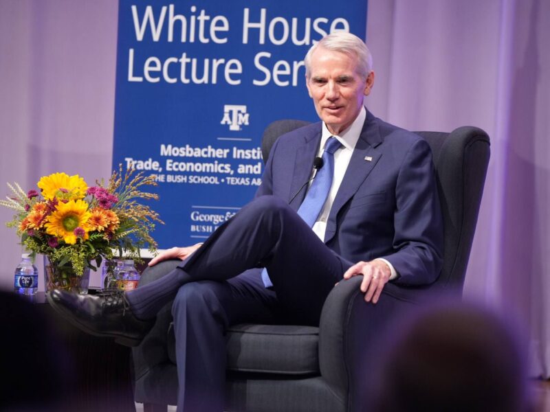 A photo of former U.S. Sen. Rob Portman sitting in a chair on a stage while wearing a suit.