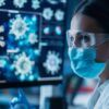 A photo of a scientist wearing a mask, goggles and lab coat while looking at images of disease cells.