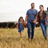 A rural family — a man, woman and two young children — walking in a pasture with cattle in the background.