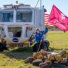 A photo of a woman planting a Texas A&M University flag in a field of grass with NASA vehicles around her.