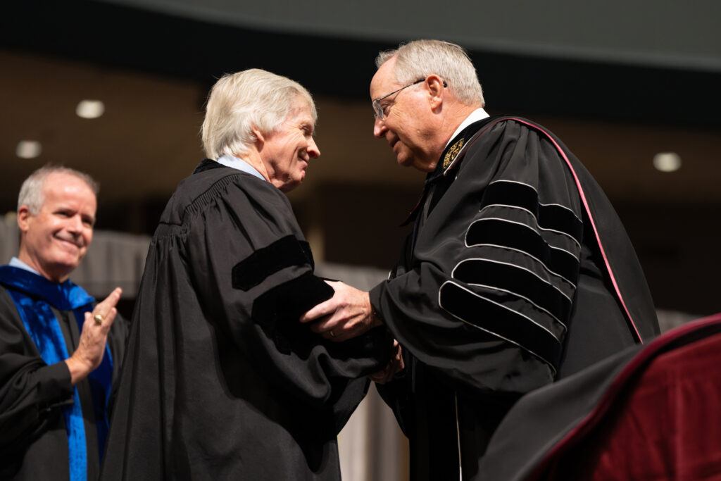 A photo of Texas A&M University President Gen. (Ret.) Mark A. Welsh III shaking hands with former U.S. Ambassador Ryan Crocker during a commencement ceremony at Texas A&M University.