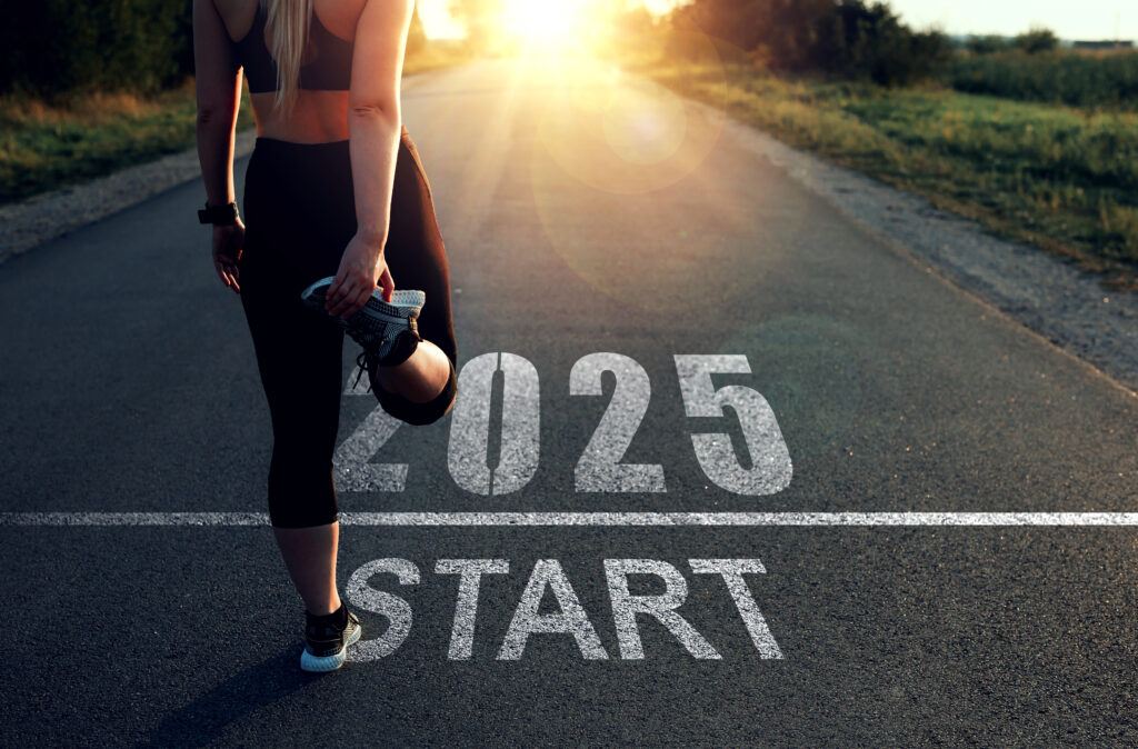 A runner stretching on a road with the words 2025 Start at her feet and a sunrise in the distance.