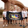 A photo of six members of Texas A&M University's Corps of Cadets standing near the Quad arches while holding a flag for the Special Operations Warrior Foundation.