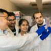 A photo of a group of researchers in lab coats looking at a sample from a lab experiment.