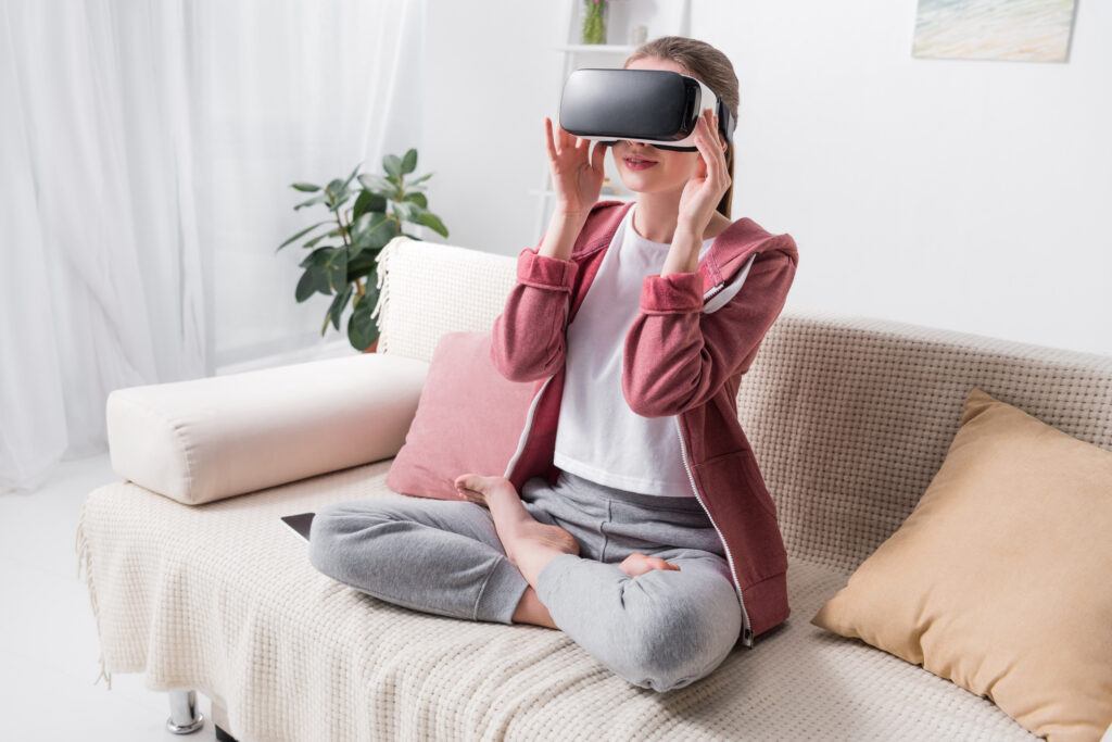 A woman sitting on a couch while wearing a virtual reality headset.