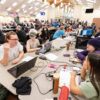 Students sit at tables with laptops during a gaming competition.