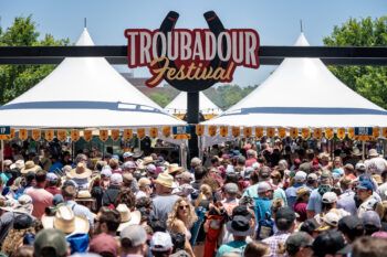 A photo of a crowd of people under a sign that says a Troubadour festival.