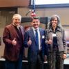 A photo of three people standing in business attire giving the Texas A&M 