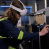 A woman wears a virtual reality headset while performing tasks in a laboratory setting.