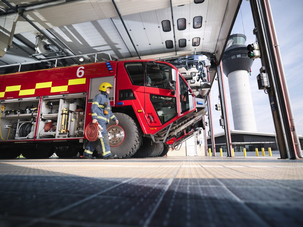 A photo of a firefighter carrying equipment to a fire engine in an airport fire stations.