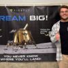 A photo of a Texas A&M student standing in front of a sign for Firefly Aerospace.