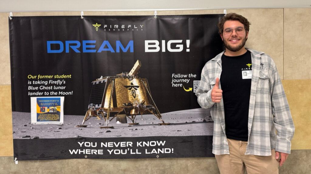 A photo of a Texas A&M student standing in front of a sign for Firefly Aerospace.