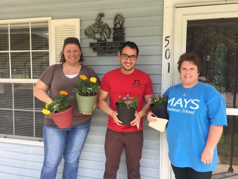 Three people pose holding potted flowers