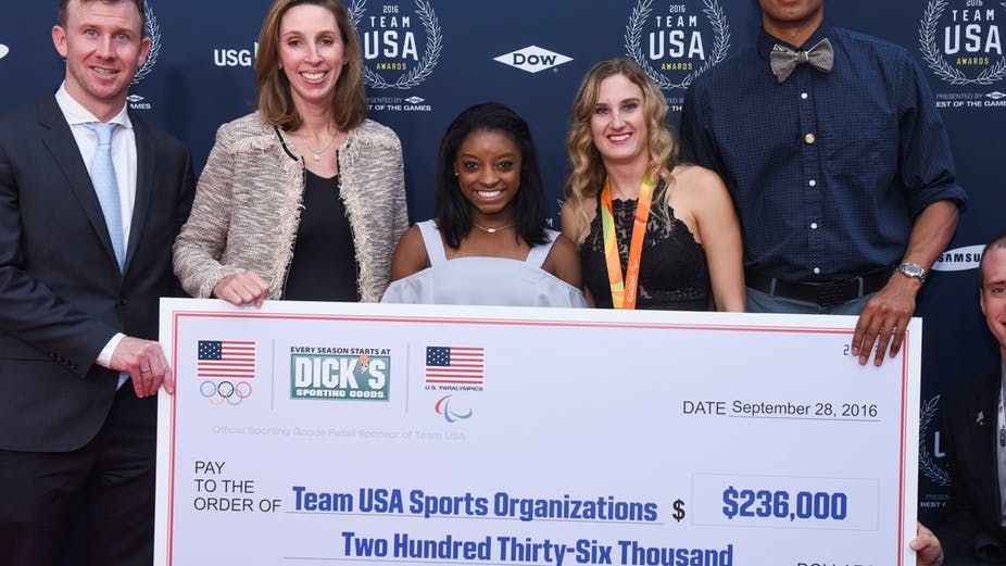 Dick’s Sporting Goods presenting Team USA – including Olympic gymnast Simone Biles – a check for $236,000. Kevin Wolf/AP Images