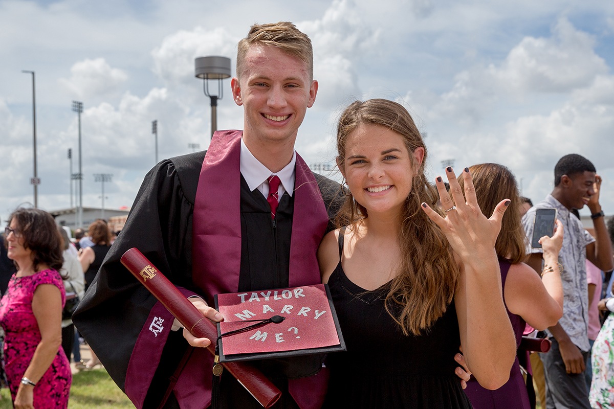 Aggies Jonathan Cox and Taylor Hepburn after summer commencement. Hepburn is showing her engagement ring and Cox is posing with his now famous cap.