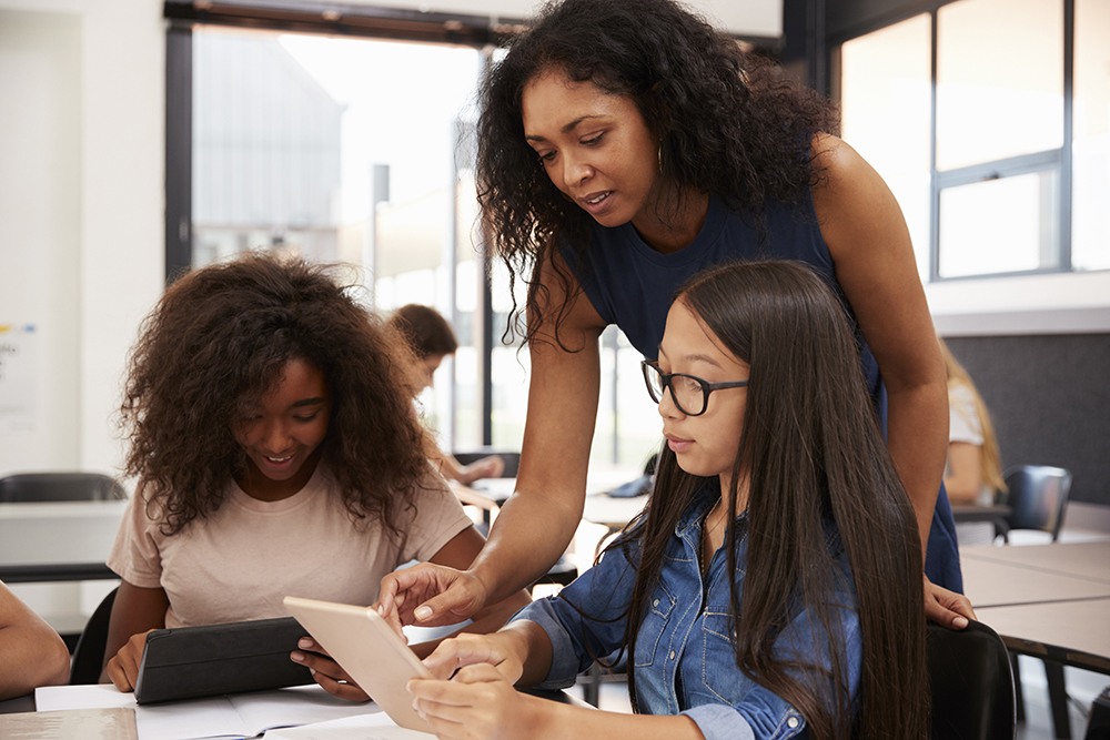 Teacher helping high school students with technology. (iStock)
